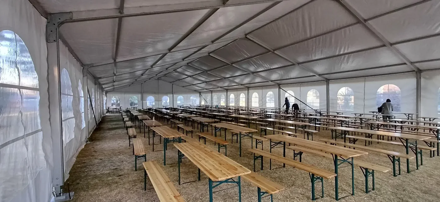 Rows of wooden beer bench tables and benches arranged inside a large marquee