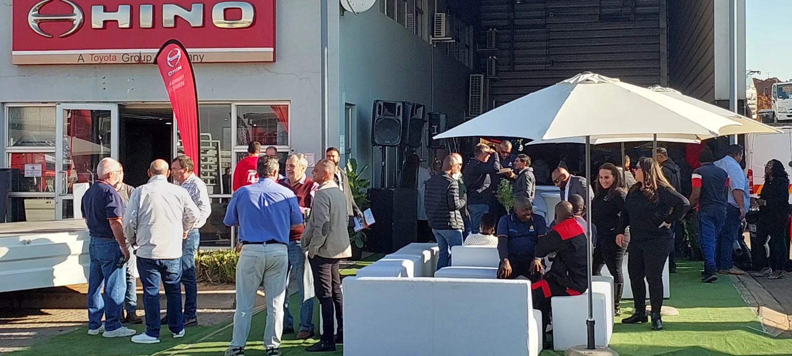 Guests gathered around white lounge furniture and a garden umbrella at an outdoor corporate event