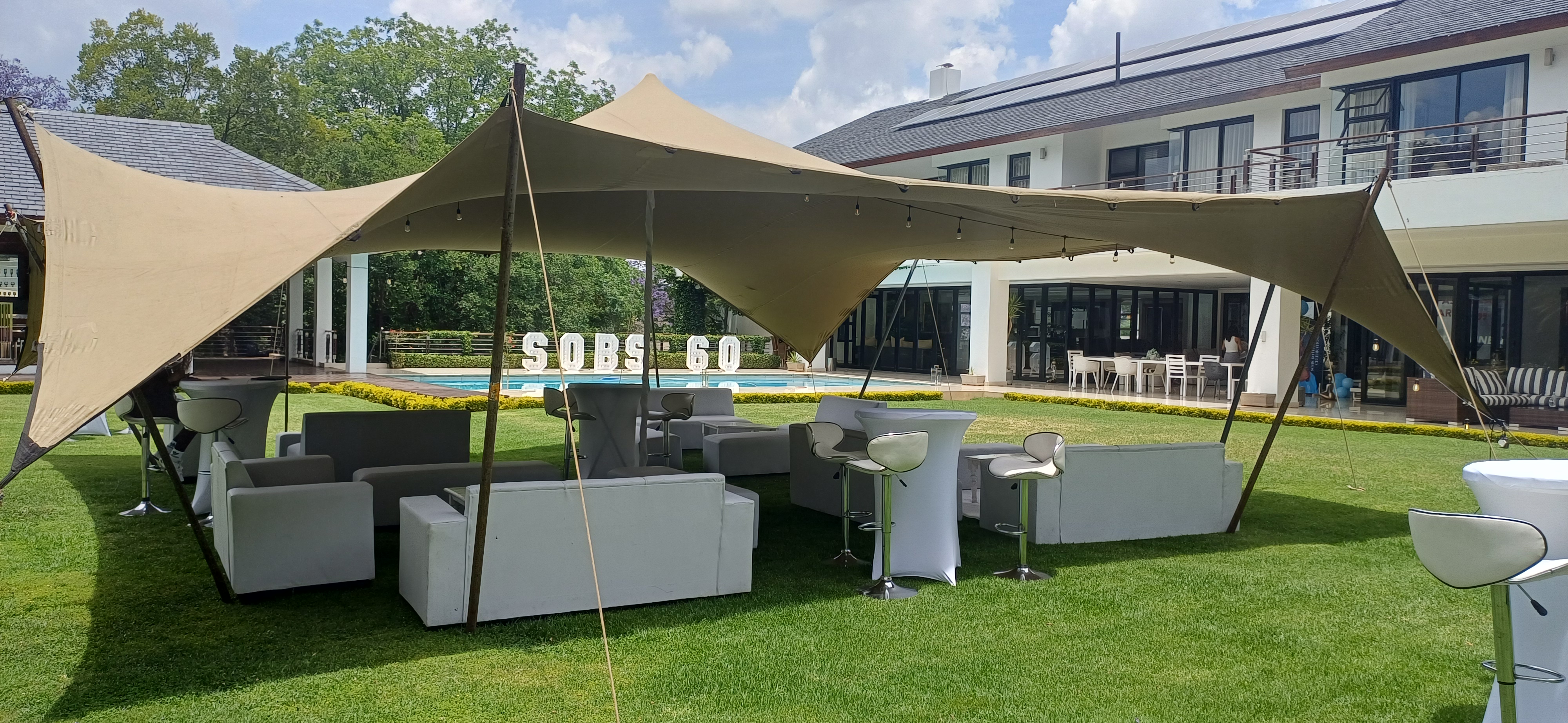 Beige stretch tent with string lights, white lounge furniture and cocktail tables at a poolside garden event